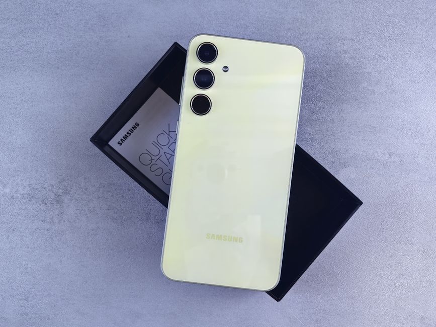 A close-up image of a sleek, modern white Samsung smartphone with a glossy finish, featuring three camera lenses aligned vertically on the top left corner and a subtle Samsung logo near the bottom cen
